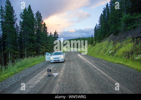 Auto su una strada di ghiaia, crepuscolo, un multicopter pronti per il decollo Foto Stock