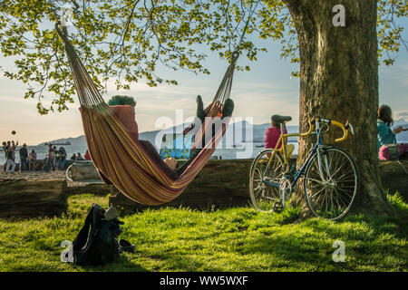 Uomo che lavora sul computer portatile in un'amaca, in corrispondenza di un albero la bicicletta, digital nomad, Vancouver, British Columbia, Canada Foto Stock