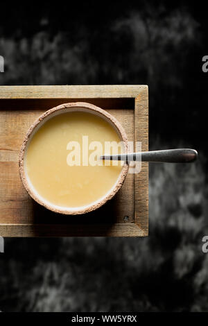 Elevato angolo di visione di un vaso di terracotta con acqua calda zuppa su un vassoio in legno, contro uno sfondo grigio scuro Foto Stock