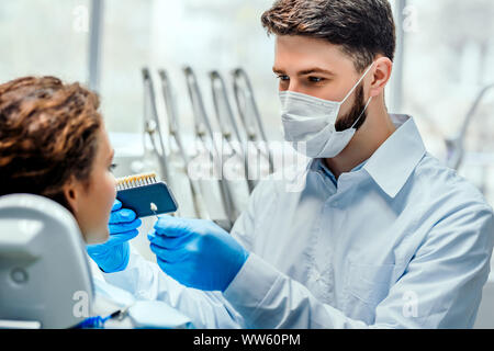 Dentista selezionando denti del paziente di colore con la tavolozza in clinica. Vista laterale. Foto Stock