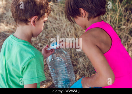 Due bambini di prelevare il cestino nella foresta. Il volontariato, carità, compiti di scuola e concetto di ecologia. Foto Stock