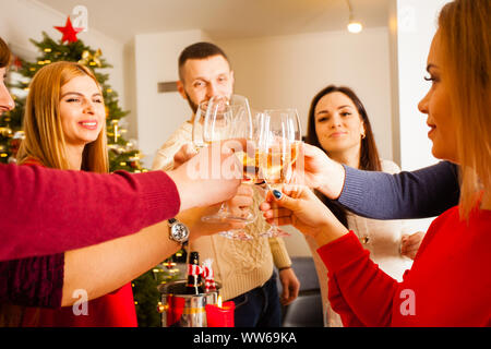 Chiudere la vista immagine che mostra un gruppo di amici per celebrare il nuovo anno, tenendo i bicchieri con lo champagne tintinnio tra di loro. Albero di natale sullo sfondo Foto Stock