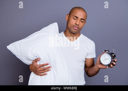 Close up photo malati mad malsana pelle scura egli lui suo macho testa calva tenere premuto CLOCK dormire a cuscino e a piedi notte insonne indossando t-shirt bianco outfit Foto Stock