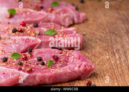 Carne di maiale cruda bistecche cosparso con spezie e erbe aromatiche. Succose bistecche di greggio per un barbecue, vicino. Foto Stock