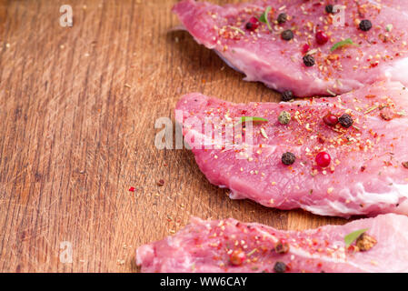 Carne di maiale cruda bistecche cosparso con spezie e erbe aromatiche. Succose bistecche di greggio per un barbecue, vicino. Foto Stock