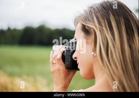 Al di sopra della spalla del giovane professionista fotografo femmina per scattare delle foto al di fuori in natura. Foto Stock