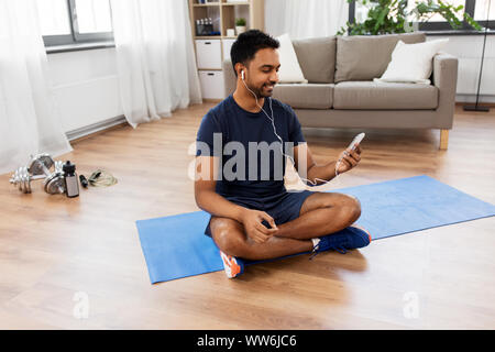 Uomo indiano con lo smartphone sul tappeto di esercizio a casa Foto Stock