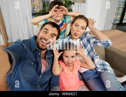 Famiglia tenendo selfie e rendendo volti a casa Foto Stock