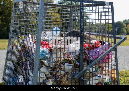 Berlino, Germania - 11 settembre 2019: Cestino pieno può / bidone dei rifiuti nel parco pubblico Hasenheide a Berlino. Riempito principalmente con immondizia di plastica Foto Stock