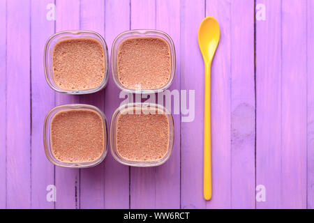 Lay piatto - Cioccolato al latte dessert su un viola sullo sfondo di legno. Quattro porzioni e giallo cucchiaio. Foto Stock