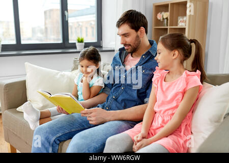 Padre felice con le figlie del libro di lettura a casa Foto Stock