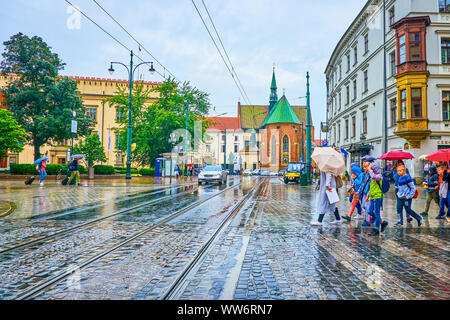 Cracovia in Polonia - Giugno 13, 2018: Il gruppo di bambini sotto gli ombrelloni attraversare la strada in tutti i Santi Square durante il giorno di pioggia, il 13 giugno a Cracovia Foto Stock