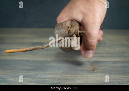 Maschio di mano che tiene il vecchio arrugginito impugnature e piegato lungo corroso chiodo su una tavola in legno rustico in una vista ravvicinata Foto Stock