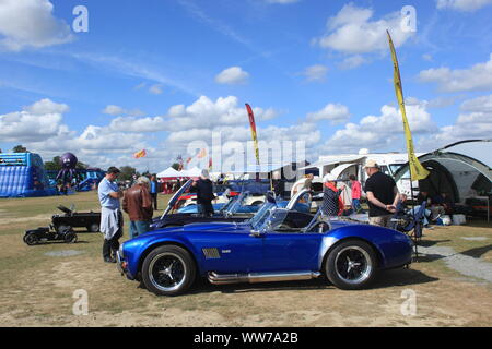 I visitatori in occasione di un evento guardando un AC Cobra Kit anglo-americano auto e altri veicoli sul display nel Kent, Regno Unito. Estate 2019. Foto Stock