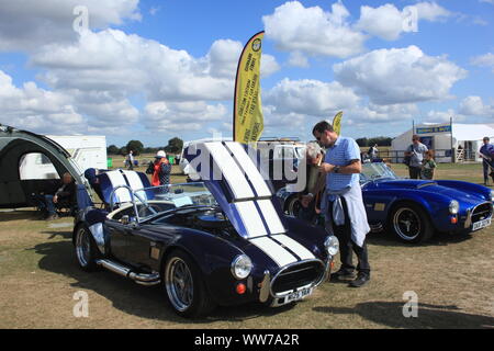 I visitatori in occasione di un evento guardando un AC Cobra Kit anglo-americano auto e altri veicoli sul display nel Kent, Regno Unito. Estate 2019. Foto Stock