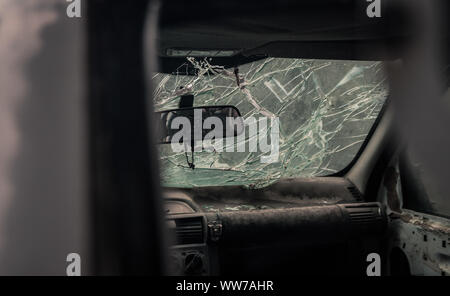 Vista dall'interno di un'auto con parabrezza frantumato. La rottura dei cristalli e i danni interni suggeriscono un recente incidente o un atto vandalico. Foto Stock