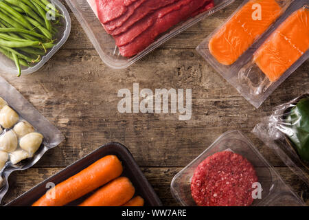 Diversi tipi di alimenti confezionati. Carne, fagiolini, carote e salmone su un tavolo di legno. Vista dall'alto. Spazio di copia Foto Stock