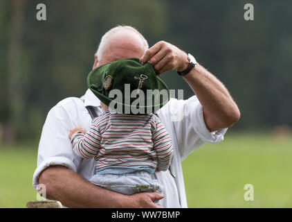 Viehscheid' dopo Almabtrieb (cerimoniale la guida verso il basso del bestiame dai pascoli di montagna nella valle in autunno) nella tarda estate in Baviera, il nonno ha un nipotino sul suo braccio, gioca con il feltro hat Foto Stock