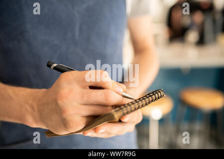 Mano del cameriere grembiule penna a sfera di contenimento sulla pagina del Blocco note mentre si lavora Foto Stock