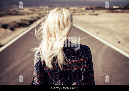 Bionda bella ragazza camminare e andare su una lunga strada diritta all'aperto a scoprire e a vivere la sua vita al top. Il vento nei capelli, la libertà e la nozione di decisione di seguire i sogni e progetti fortemente Foto Stock