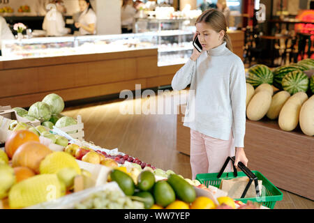 Pretty girl in informale a parlare con la sua mamma sul telefono cellulare dal display di frutta Foto Stock