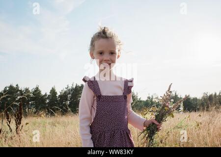 Ritratto di una giovane ragazza la raccolta di fiori di campo in un prato al tramonto Foto Stock