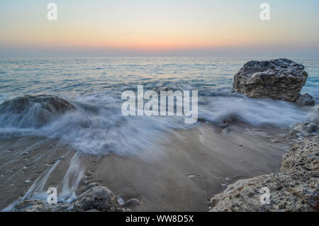 Le onde dopo il tramonto, lattiginoso onde in twilight su sabbia e alcune rocce su una spiaggia, lunga expositure Foto Stock