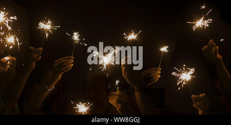 Notte oscura celebrare il concetto con molte mani che prendono e utilizzando la luce brilla fire insieme hanno divertimento per capodanno o partito, compagnia e amicizia durante la celebrazione di uno stile di vita felice Foto Stock