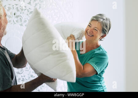 Cuscini guerra in casa per la caucasian paio di giocoso senior adulto uomo e donna giocare in camera al mattino, felicità e gioia insieme per sempre restare giovane senza limiti di età, ridere un sacco e godendo l'attività a casa Foto Stock