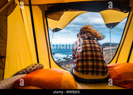 Bella donna vista dal retro seduta al di fuori di una tenda montata su di un'auto. outdoor vacanza libertà concetto alternativo cercando ocean fuori porta. sensazione mare e avventura Foto Stock