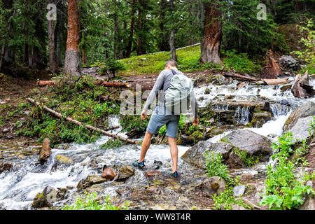 L'uomo Varcando il fiume su enigma Creek Trail in Aspen Colorado nel 2019 arrampicate estive con rocce umide dopo snowmelt Foto Stock