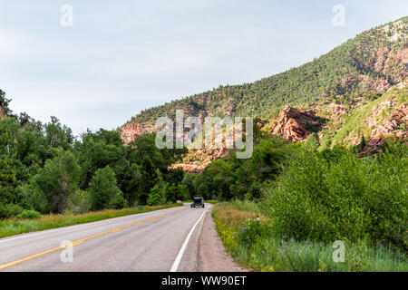 Vista di rocky red cliff dalla strada autostrada 133 in Redstone, Colorado durante il periodo estivo con alberi in sera la luce del sole e automobili Foto Stock