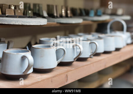 Vetri piatti di ceramica stand su un ripiano in officina scaffalature con ceramiche fatte a mano e tazze di argilla. Foto Stock