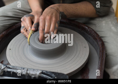 Il master crea prodotti da argilla grigia su un tornio del vasaio. Ragazza crea un vaso di ceramica. Foto Stock