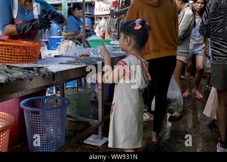 Bambino che usa il suo dito per ordinare un articolo da un fornitore di pesce. Mercato di strada della Thailandia. Shopping per bambini Foto Stock