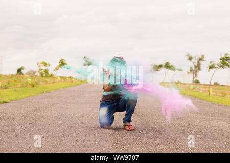 Concetto di holi festival, uomo esplosione di polveri colorate in mani su strada. Foto Stock