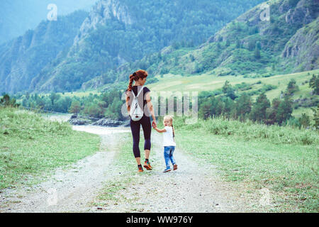 Madre e figlia sono tra le montagne su una strada di campagna con la mano Foto Stock