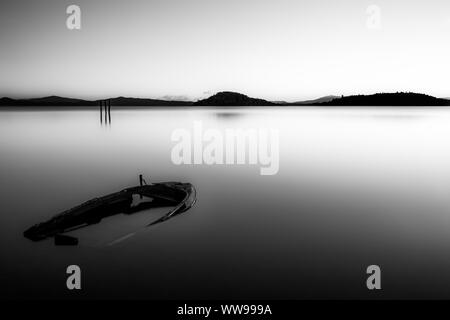 Un quasi completamente assorbita piccola barca nel lago Trasimeno (Umbria, Italia) al tramonto Foto Stock