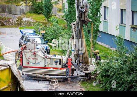 Espoo, Finlandia: calore geotermico installazione pompa in Eco Friendly apartment house. Impianto di perforazione in cantiere. Lavoratore in hard hat la perforazione di un pozzo di trivellazione Foto Stock