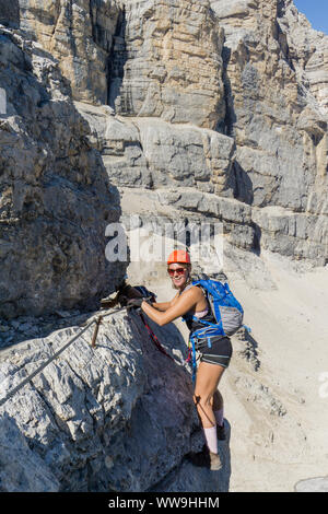 Attraente femmina bruna alpinista su esposta una Via ferrata in Alto Adige divertendosi e sorridente Foto Stock