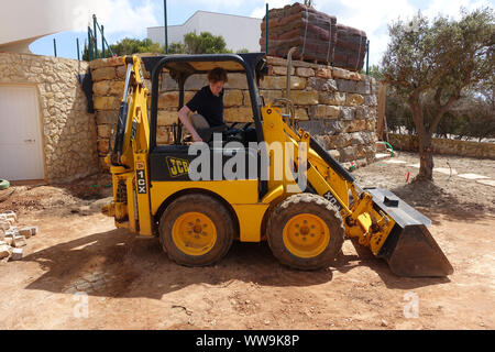 Algarve Portogallo 10 Aprile 2019: UN JCB mini escavatore essendo utilizzato per fare lavori paesaggistici in un giardino frontale Foto Stock