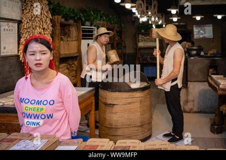 Xian, Cina - Luglio 2019 : due uomini difficile colpire con grossi martelli di legno per il crack grano che verrà utilizzato nella realizzazione di snack dolce per la vendita su str Foto Stock