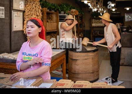 Xian, Cina - Luglio 2019 : due uomini difficile colpire con grossi martelli di legno per il crack grano che verrà utilizzato nella realizzazione di snack dolce per la vendita su str Foto Stock