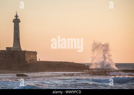 Faro a Rabat, Marocco durante il tramonto con grandi onde si infrangono. Foto Stock