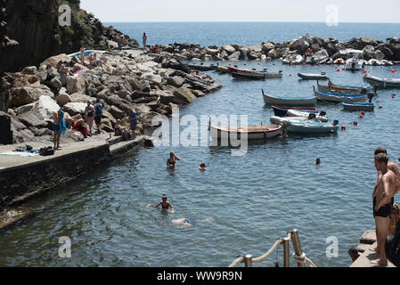 Riomaggiore, Italia - Luglio 2, 2018: Su un caldo a metà giornata estiva, bagnanti nuotare tra le barche ormeggiate a Riomaggiore, una delle cinque attività di pesca tradizionale vi Foto Stock