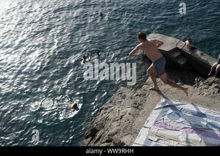Manarola, Italia - Luglio 2, 2018: un turista corre verso il bordo di una scogliera di tuffarsi in mare su un caldo a metà giornata estiva in Cinque Terre. Foto Stock