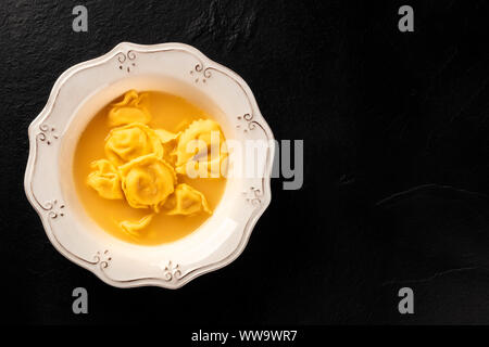 Italian tortellini in brodo, overhead shot su uno sfondo nero con copyspace Foto Stock