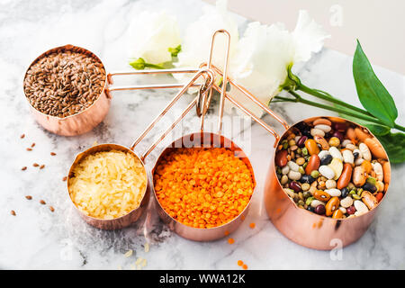 Rame tazze di misura sulla tavola di marmo con fagioli e cereali in cucina. O di cottura di alimenti sfusi concetto di acquisto Foto Stock