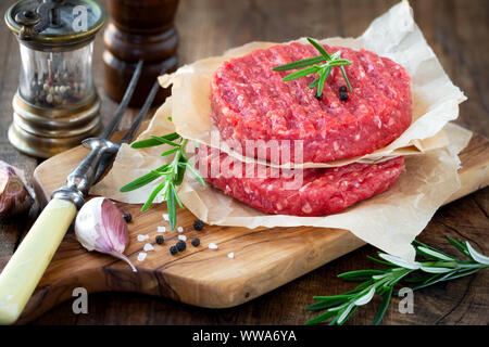 Materie tritare carne Hamburger di carne su un tagliere di legno con rosmarino fresco, i chiodi di garofano di aglio e pepe i duroni e sale Foto Stock