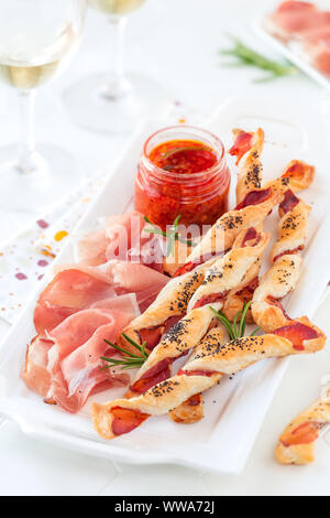 Il pane fatto in casa bastoni con affumicato Prosciutto stagionato servito come antipasto con fette di prosciutto e vino su una piastra bianca Foto Stock